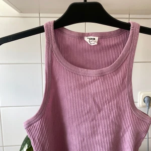 Lila ribbad linnetopp från Monki - Säljer en superfin lila ribbad topp. Perfekt för sommardagar eller som ett lager under en mysig kofta. Toppen är ärmlös och har en skön passform. Passar både till vardags och fest! 💜