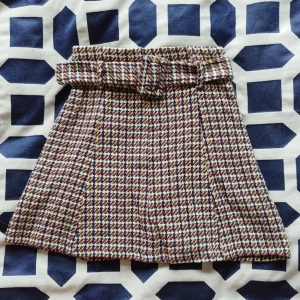Rutig kjol med bälte - Säljer en superfin rutig kjol med ett matchande bälte. Kjolen har ett klassiskt mönster som är perfekt för höst och vinter. Den är i en kort modell och har en chic och stilren look. Perfekt för både vardag och fest! - aldrig använd