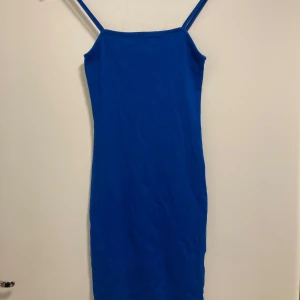 Blå klänning från Amisu - Säljer en snygg blå klänning från Amisu i storlek EU 34. Den är ärmlös med smala axelband och har en enkel, stilren design. Perfekt för sommardagar eller en festlig kväll. Materialet känns mjukt och bekvämt mot huden.