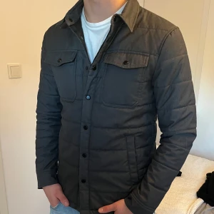 Grå jacka från Zara - Säljer en snygg grå jacka från Zara i storlek S. Perfekt för höst och vår, med en stilren look som passar till det mesta. Den har två bröstfickor med knappar och sidfickor. Helt ny