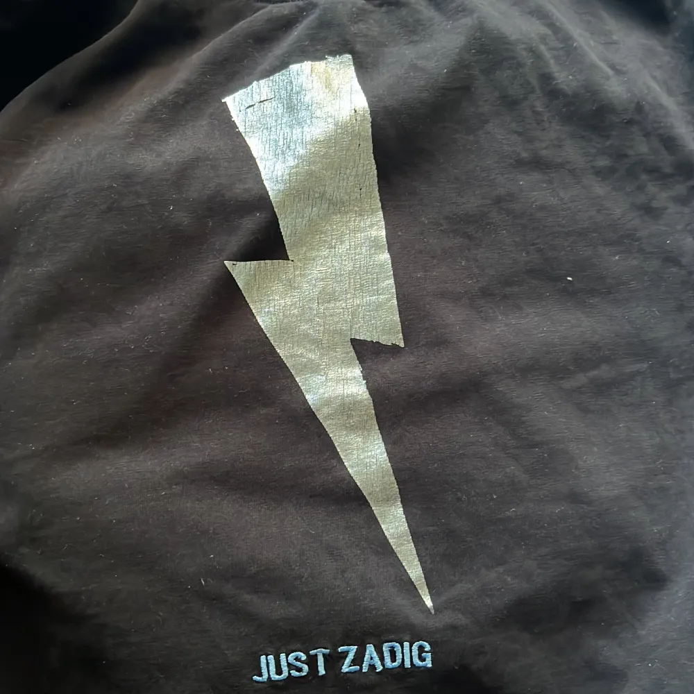 Säljer en cool svart t-shirt från Zadig & Voltaire med en stor blixt i silver på framsidan och texten 'JUST ZADIG’. Storlek m men passar också s! Säljer då den inte kommer till användning längre💞💞. T-paidat.