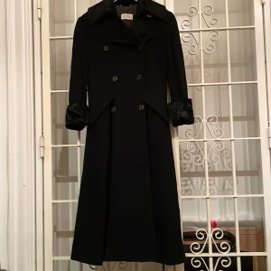 Svart ullkappa - Svart kappa i ull med slag och ärmslut i pälsimitation. Kappan är i storlek 34 men rymlig så även storlek 36 fungerar. Kappan är i gott skick, dock en liten reva i innerfodret, se bild