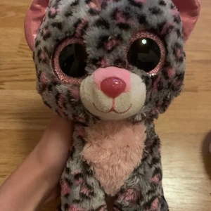 Gosig leopardmjukisdjur - Supergullig leopardmjukis med stora glittriga ögon och rosa detaljer. Den har en mjuk, grå päls med svarta och rosa fläckar, och en söt rosa nos. Perfekt för kramar och mysiga stunder!