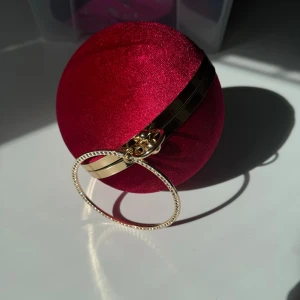 Röd rund kuvertväska med gulddetaljer - Nyskick! Säljer en supercool röd rund kuvertväska i sammet med gulddetaljer. Väskan har ett glittrigt handtag som gör den perfekt för fest. Insidan är svart och det finns en kedja för att bära den över axeln. Hämtas på Hägerstensåsen eller ök. 