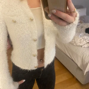 Vit fluffig kofta från Amisu - Säljer en supermysig vit fluffig kofta från Amisu. Den har snygga guldfärgade knappar och är perfekt för att hålla sig varm och stilren. Koftan är i storlek S och passar perfekt för både vardag och fest. Den är i nyskick och redo för en ny garderob!