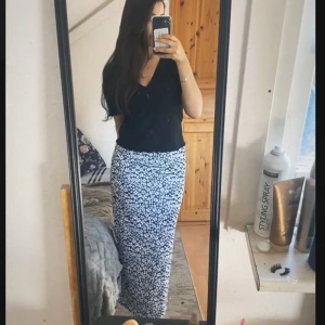 Blommig långkjol - Säljer en superfin långkjol med blommigt mönster i svart och vit. Kjolen har en rak passform med en slits vid sidan . Den är gjord i ett lätt och bekvämt material, storlek M men passar även S