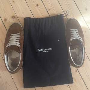 Säljer ett par snygga bruna sneakers från Saint Laurent. De är i mocka och har en klassisk design med vita snören och en vit sula. Skorna är i ett helt ok skick. Mycket använda. Sulorna är i dåligt skick men utsidan på skon helt ok. 