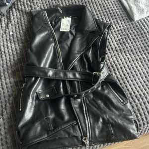 Skinn väst  - En väst material av skinn, aldrig använd, storlek XXS, västen är vegan. Den har en bälte med med silver hål på.