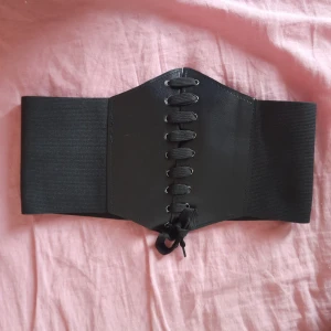 Svart korsettbälte - Säljer ett snyggt svart korsettbälte med snörning framtill. Bältet har en bred elastisk design som ger en bekväm passform och en cool look. Perfekt för att ge extra stil till vilken outfit som helst!