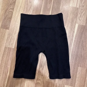 Svarta ribbade cykelshorts - Svarta ribbade cykelshorts. De är högmidjade och har en tight passform, perfekta för träning eller en avslappnad dag. Materialet är stretchigt och bekvämt. Från Hoxton Haus i storlek M-L. Helt onavända!! 