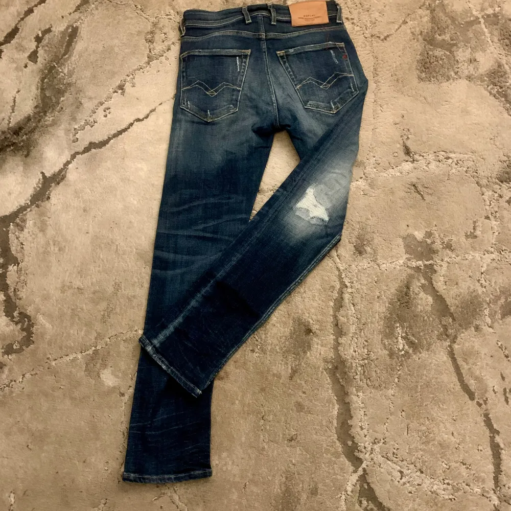 Säljer ett par snygga blå jeans från Replay. De har en cool slitningseffekt och en klassisk femficksdesign. Jeansen är i en mörkblå tvätt med ljusare partier och slitningar på framsidan och baksidan. Perfekta för en avslappnad stil! Passform; Grover . Jeans & Byxor.