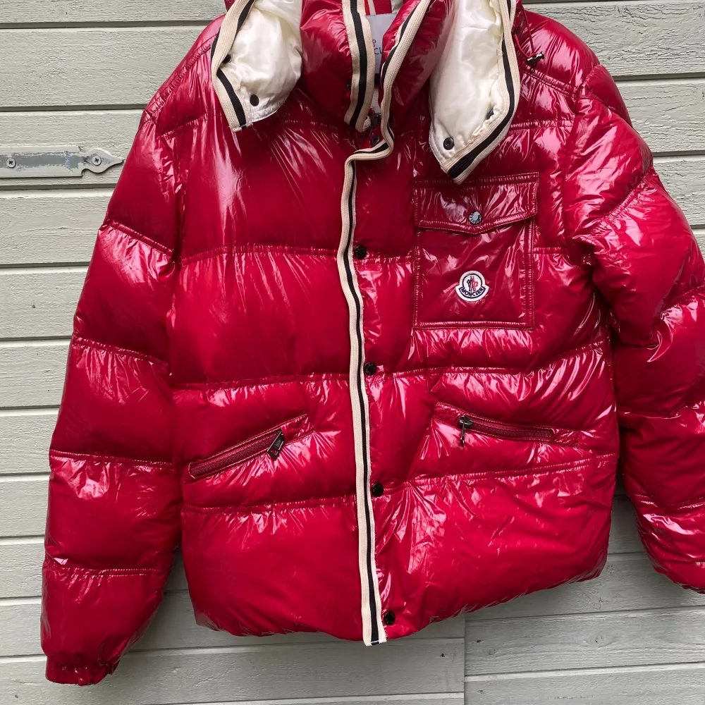 Säljer en snygg röd pufferjacka från Moncler. Jackan har en glansig finish och är perfekt för kalla dagar. Den har en avtagbar huva med tryckknappar och en cool serietidningsdetalj på insidan. Dragkedjorna är robusta och det finns flera praktiska fickor. Perfekt för vintern! 🔥. Jackor.