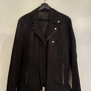 Svart skinnjacka från Filippa K - Säljer en snygg svart skinnjacka från Filippa K i storlek 52. Jackan har en cool design med dragkedjor och knappar som detaljer. Perfekt för höst och vår, och ger en stilren look till vilken outfit som helst. Passar både till vardags och fest!