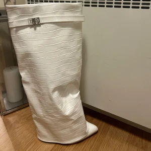 Vita stövlar med bälte - Säljer ett par stilrena vita stövlar med en snygg bältesdetalj upptill. De har en spetsig tå och är perfekta för att ge en elegant touch till din outfit. Passar bra till både vardag och fest! Aldrig använda super snygga!