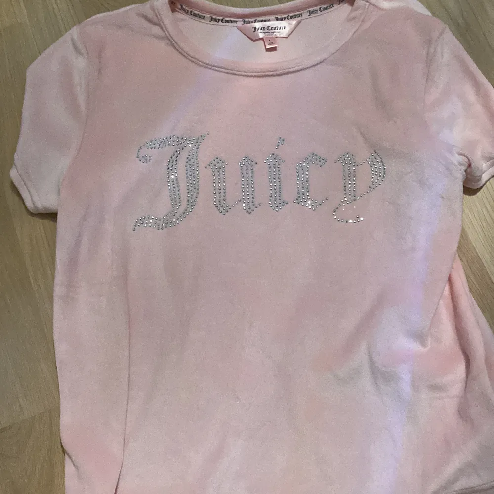 Säljer en superfin rosa t-shirt från Juicy Couture. Den har korta ärmar och är gjord i ett mjukt material. På framsidan står det 'Juicy' i glittriga bokstäver. Perfekt för en avslappnad och stilren look! Aldrig använd! Som ny!!. T-shirts.