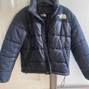 Svart pufferjacka från The North Face - Säljer en The North Face jacka. Märket på framsidan är lite missfärgat samt att det finns ett litet hål i nederkant till höger om dragkedjan. Hålet är inte så pass stort så att dun åker ut men finns där. Nypris på över 2000kr