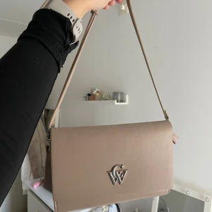 Beige Axelremsväska Carin Wester - Helt ny, utan prislapp, axelremsväska från Carin Wester. Normalpris 400kr. • Imitationsläder • Magnetlås • 2 innerfickor, en med dragkedja.  • Juster- och avtagbar axelrem  Mått: Längd: 23 cm Höjd: 16 cm Djup: 4 cm