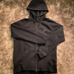 Svart hoodie från Nike - Säljer en svart Nike tech i bra skick. Perfekt för både vardag och träning. Den är superbekväm och stilren, ett måste i garderoben! Va inte rädd för att skriva om du undrar något