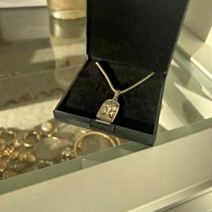 Silverhalsband med trädmotiv från Silverknappen - Säljer ett elegant silverhalsband från Silverknappen. Hänget har ett vackert trädmotiv och kommer i en snygg svart ask. Perfekt för både vardag och speciella tillfällen!