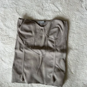 Beige korsettopp - Säljer en snygg beige korsettopp från Oh Polly. Den har en tight passform och är perfekt för festliga tillfällen. Toppen är axelbandslös och har en stilren design med markerade sömmar som ger en fin siluett.