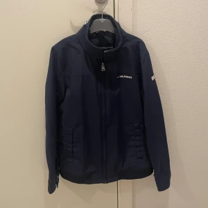 Mörkblå jacka från Tommy Hilfiger - Säljer en snygg mörkblå jacka från Tommy Hilfiger. Den har en dragkedja framtill och är långärmad. Perfekt för höst och vår med sin stilrena design och bekväma passform. Jackan har också Hilfiger-loggan på bröstet och nacken.
