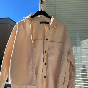 Beige manchesterjacka från Zara - Säljer en superfin beige manchesterjacka från Zara. Den har en avslappnad passform med långa ärmar och knappar framtill. Perfekt för höst och vår när du vill ha något stilrent och bekvämt. Jackan har en bröstficka som ger en extra touch. Passar till både vardag och lite mer uppklädda tillfällen!