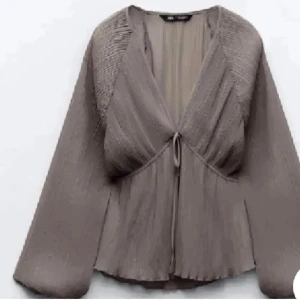 Brun blus med knytning - Säljer en superfin brun blus med knytning framtill. Den har långa ärmar och ett luftigt, plisserat tyg som ger en elegant look. Perfekt för både vardag och fest!