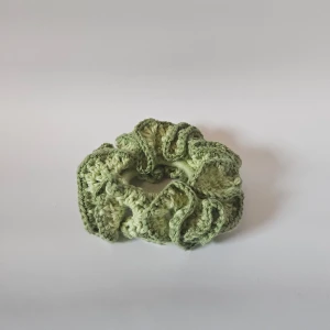 Grön stickad scrunchie - Säljer en superfin grön virkad scrunchie som är perfekt för att piffa upp vilken frisyr som helst. Den är mjuk och elastisk, vilket gör den bekväm att bära hela dagen. Perfekt accessoar för både vardag och fest!