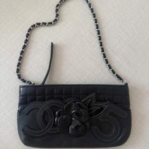 Rare vintage Chanel mini bag in lambskin. The exterior features a playful embossed design combining matte and patent leather, showing iconic Chanel symbols: the interlocking C, the camellia flower, and the number 5. Beneath this embellishment is a di