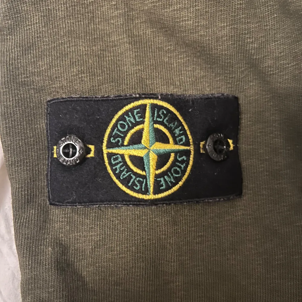 Säljer en snygg olivgrön tröja från Stone Island. Den har en klassisk rund hals och långa ärmar. På ärmen finns det ikoniska Stone Island-märket. Perfekt för en stilren och avslappnad look!. Tröjor & Koftor.