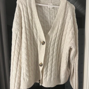 Vit stickad kofta från H&M - Säljer en supermysig vit stickad kofta från H&M. Den har ett snyggt flätmönster och stora knappar framtill. Använd ett fåtal gånger.