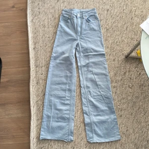 Ljusblå vida jeans - Säljer ett par ljusblå byxor med hög midja och vida ben. De har en klassisk femficksdesign med knapp och dragkedja framtill. Perfekta för en avslappnad stil och passar till både vardag och fest!