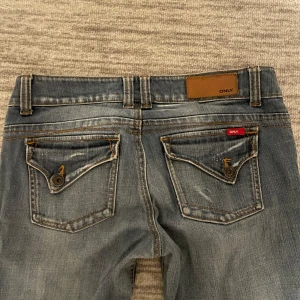 Lågmidjade jeans från Only - Snygga blå jeans från Only med en klassisk femficksdesign och knappdetaljer på bakfickorna. 