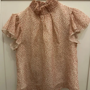 Blommig blus från Shein - Söt blommig blus från Shein i beige. Blusen har korta volangärmar och en hög krage med smockdetaljer. Perfekt för en somrig look!🌼🌸😊