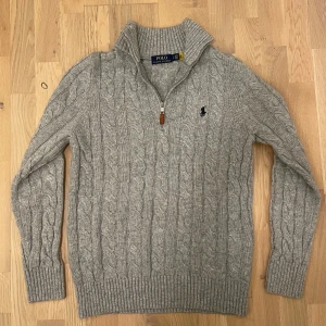 Ralph lauren half zip - Säljer en stilren grå stickad tröja från Polo Ralph Lauren med kabelstickat mönster och dragkedja vid halsen. Tröjan har långa ärmar och en broderad logotyp på bröstet. Perfekt för kyliga dagar! Passar dig med storlek S! Priset är diskuterbart