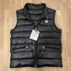 Moncler GUI väst - Säljer nu min Moncler GUI väst som är i nyskick nästan aldrig använd. Storlek 3/L men passar S/M. Själv bär jag S i alla plagg och är 170 lång då den passar perfekt. Färg svart med lite glans vid köp får du med triangel och tags som satt på från köpet. Perfekt nu när vintern börjar bli mildare! Priset är diskuterbart