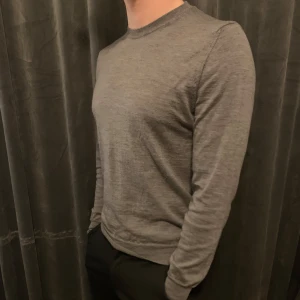 Grå tröja från Oscar Jacobson 100% merinoull  - Säljer en stilren grå tröja från Oscar Jacobson i 100% merinoull. Tröjan har en klassisk design med rund hals och långa ärmar, perfekt för en elegant look. Passar bra till både vardag och mer formella tillfällen.