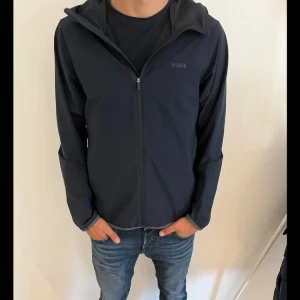 Mörkblå jacka från Boss - Snygg mörkblå jacka från Boss med dragkedja framtill. Jackan har en stilren design med långa ärmar och en bekväm passform. Perfekt för en casual look. Perfekt för den kommande våren 