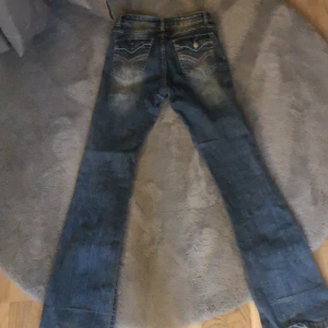 Blå jeans med broderade bakfickor o toning  - Snygga blå jeans med bootcut-stil och broderade detaljer på bakfickorna. De har en klassisk femficksdesign och en lätt tvättad look. Perfekta för en avslappnad stil.