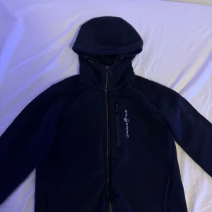Svart zip tröja  från Sail Racing - Säljer en svart tröja  från Sail Racing med huva och dragkedja. Jackan har en stilren design med en liten logotyp på bröstet. Perfekt för kyligare dagar. Storlek xs skick 8/10 inte så använd eftersom den var lite för liten för mig. köpt på pondus för 1499kr  pris kan diskuteras 