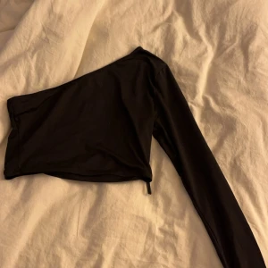 Svart oneshoulder topp - Snygg svart oneshoulder topp från shein. Perfekt för en stilren look med lång ärm och en modern design. Passar utmärkt till både jeans och kjol.