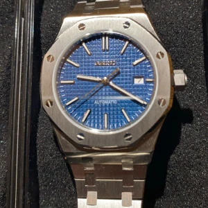 Seiko Automatisk klocka med blå urtavla -  automatisk klocka med modell efter AP klocka.en blå urtavla och datumvisning. Klockan har en robust silverfärgad boett och armband i metall. Perfekt för den som gillar en stilren och modern look.