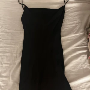 Svart axelbandslös klänning - Snygg svart klänning med smala axelband och en elegant, enkel design. Perfekt för en stilren look. Klänningen är axelbandslös och har en figurnära passform.