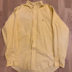 Gul skjorta från Ralph Lauren - Säljer en klassisk gul skjorta från Ralph Lauren med knappar och broderad logga på bröstet. Skjortan har långa ärmar och en stilren design som passar perfekt för olika tillfällen. Perfekt för dig som gillar en tidlös stil! 💛 Pris kan diskuteras.