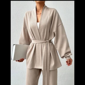 Beige set - Stilrent beige set med en kofta  och matchande byxor. Koftan har en knytning i midjan och vida ärmar, vilket ger en elegant look.