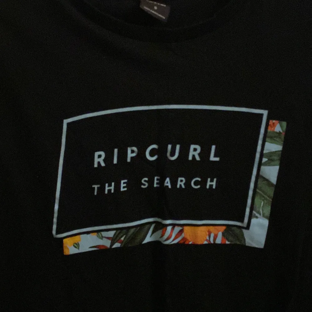 Snygg svart t-shirt från Rip Curl med tryck 'The Search' och färgglada detaljer. Perfekt för en avslappnad stil. Kortärmad och bekväm passform. I fint skick. Storlek S.. T-paidat.