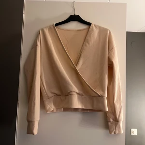 Beige omlottopp - Säljer en stilren beige omlottopp med ribbad struktur. Toppen har långa ärmar och en v-ringad design som ger en elegant look. Perfekt för en avslappnad men chic stil.