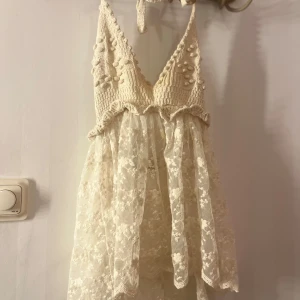 Vit spetsklänning med stickad topp - Charmig vit klänning med en stickad topp och spetskjol. Den har en v-ringad design med dekorativa detaljer på toppen och en öppen rygg. Perfekt för sommarens varma dagar. Hör av er vid intresse