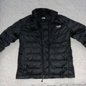 Vinterjacka  - Säljer en stilren svart dunjacka från The North Face. Jackan har en dragkedja framtill och är långärmad. Perfekt för kyligare dagar med sin quiltade design som håller värmen. En klassisk och funktionell jacka för alla tillfällen.