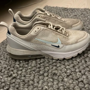 Nike sneakers  - Säljer ett par snygga Nike sneakers i beige och vit med blå detaljer. Skorna har en stilren design med snörning och en bekväm sula. Perfekta för en avslappnad stil har bara använt dom på gymmet som ett par träningsskor går att tvätta dom mer!